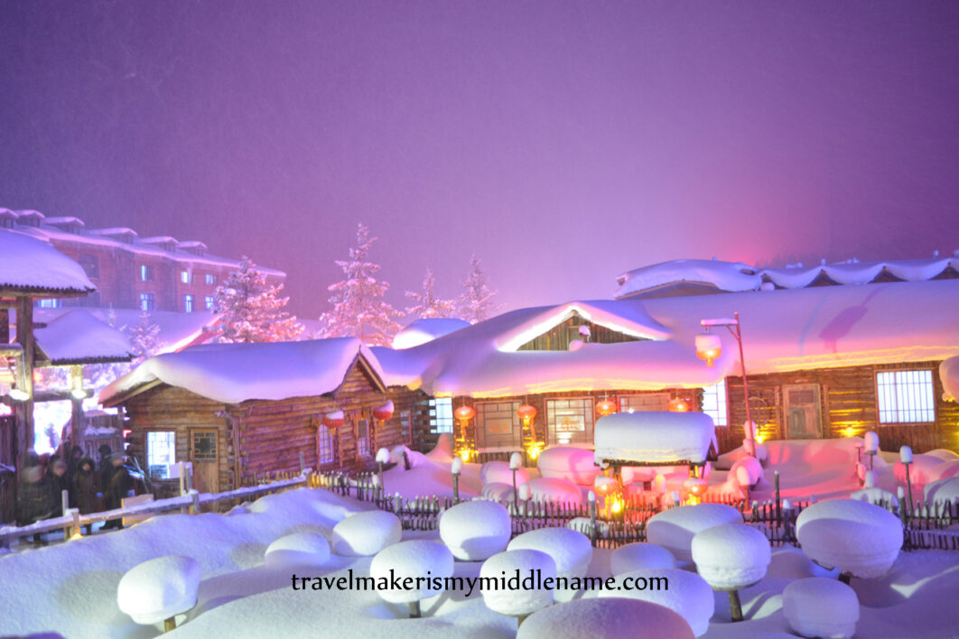 Meng Huan Jia Yuan village at night with many "snow mushrooms": round pillows of white snow that collect on top of stumps of wood, and wooden houses covered in snow looks exactly like a gingerbread house covered in sugar icing.