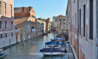 Some boats are docked along some walls at the back of a building along a canal in Venice.