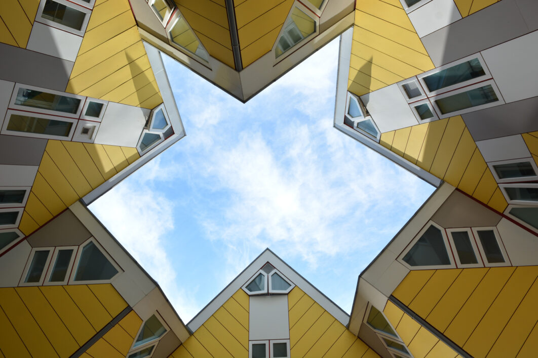 A worm's eye view of the roof line of the yellow Cube houses in Rotterdam, the Netherlands, with a star shaped gap in the middle showing a light blue sky with wispy white clouds