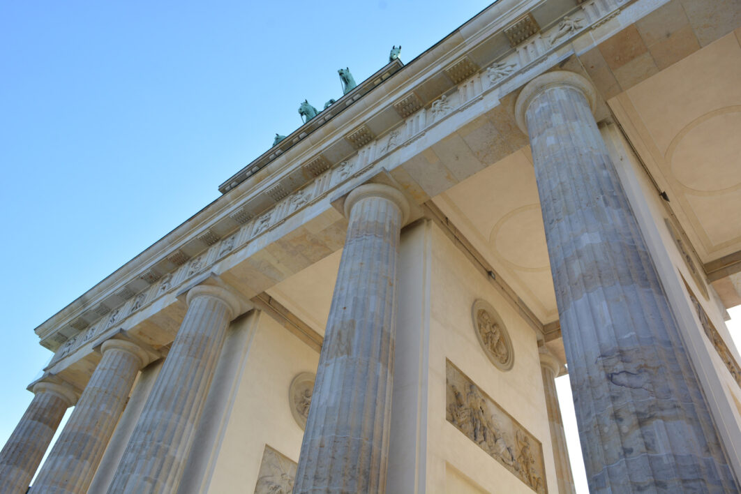 A worm's eye view of the magnificent, white Brandenburger Tor columns in Berlin against a blue cloudless summer sky.