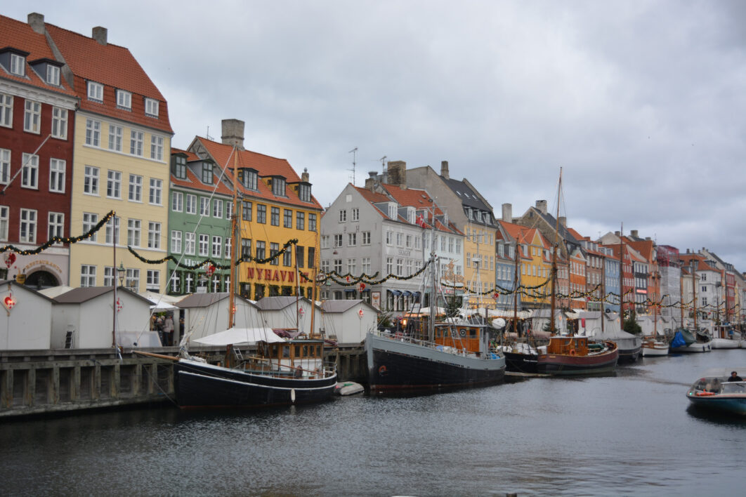 A view of the colourful buildings in Nyhavn harbour in Copenhagen on a grey winter's day with boats in front of them and dark waters in the foreground.