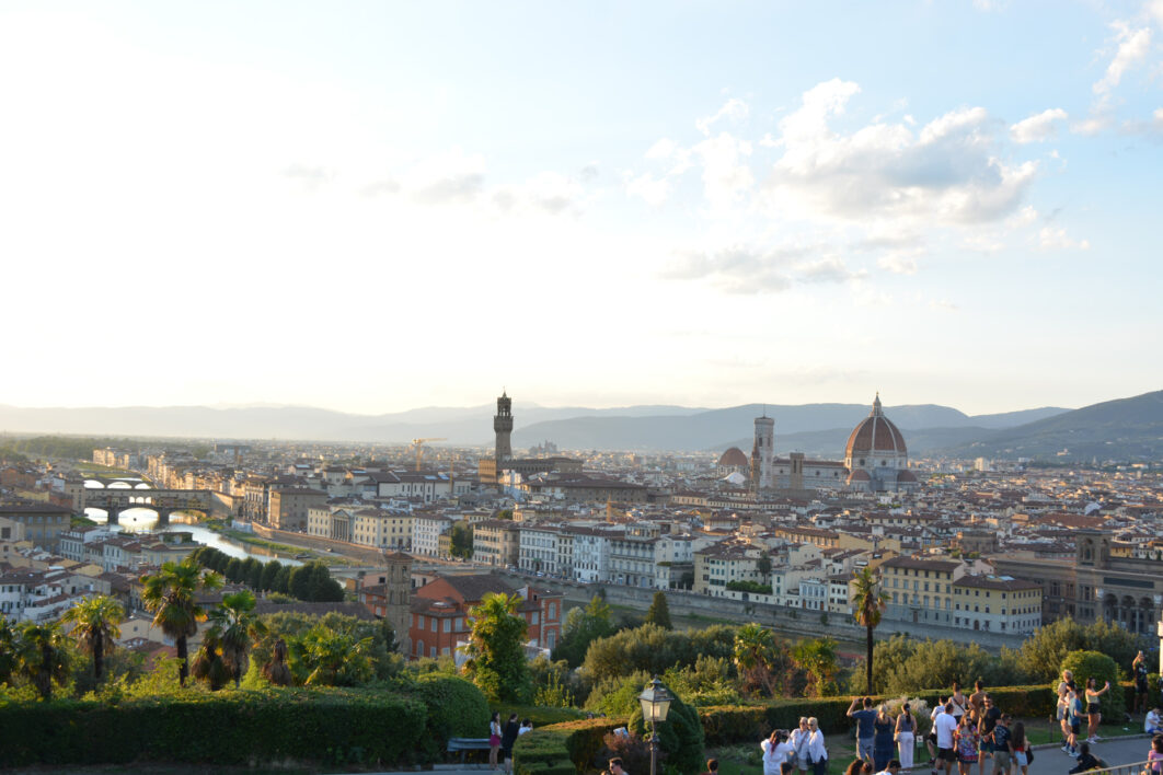 A view of Florence seen from the high elevation of the Piazza Michelangelo showing vegetation, the city, and the Duomo in the distance int the daytime.