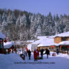 Daytime: Snow covered buildings with a forest covered mountain behind it. A few people walk through the snow covered grounds as a delivery truck slowly moves ahead.