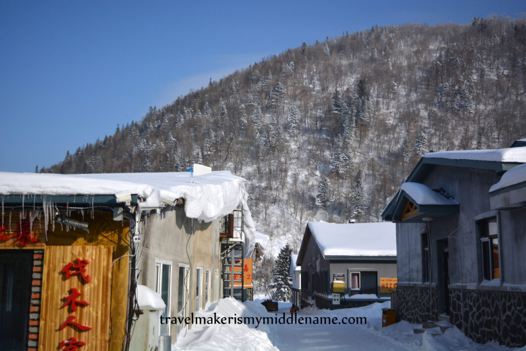 Daytime: Snow covered individual hotel rooms and buildings with forested mountains in the background.