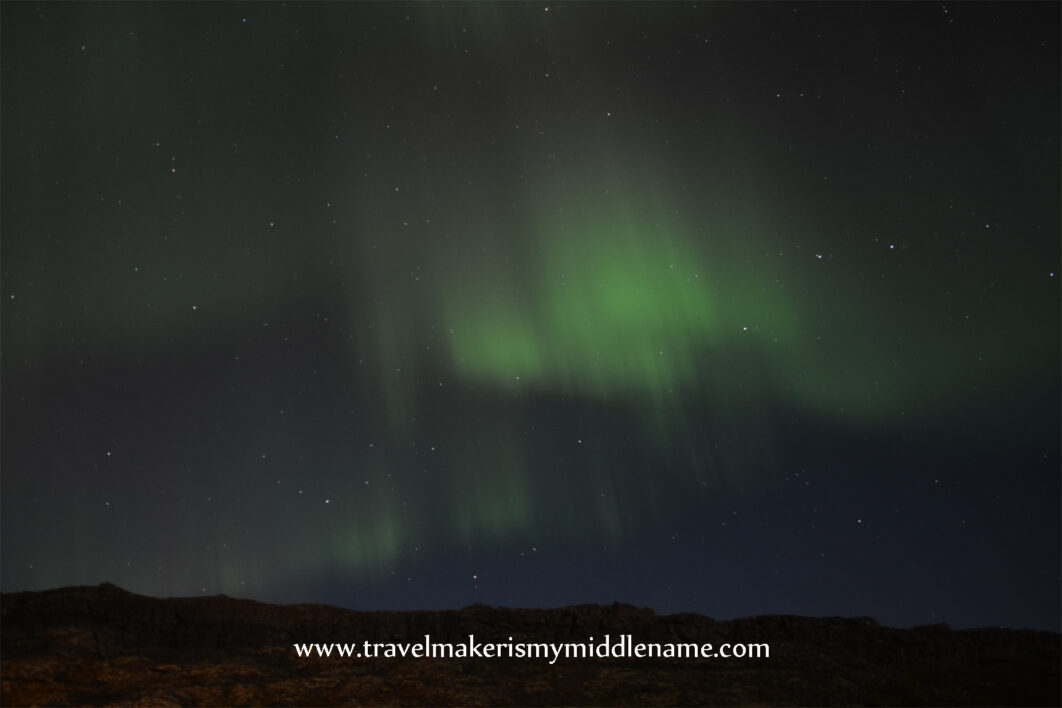 Green northern lights in the night sky with hills in the background