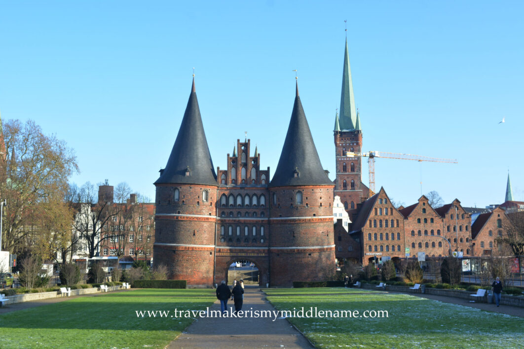 The Holstentor of Lübeck with some frost on the lawn in front. To the right in the back is the Marien church, and to the right in the front is the Salzspeicher (Salt storage) building.