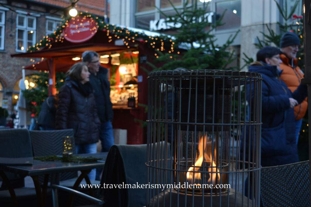 People walkig through a Christmas market in Lübeck with a warming fire in the foreground