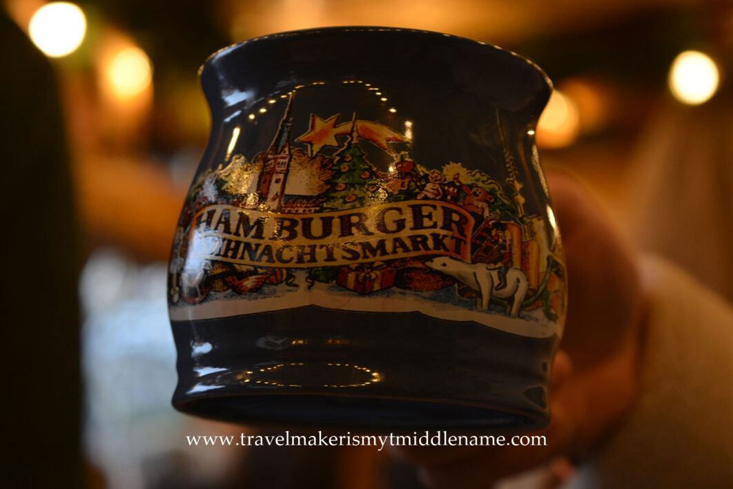 A ceramic mug with a painting of a Christmas market and the words "Hamburg Christmas market" on it in German