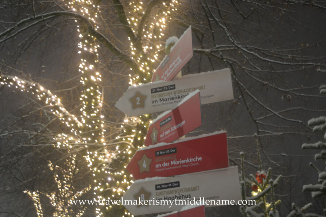 Snow covered street signs pointing in many directions directing visitors to different parts of the Christmas market in Lübeck at night