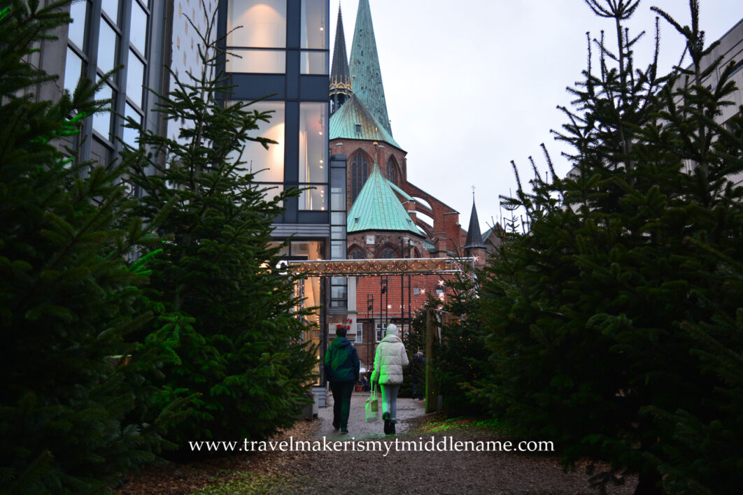 Two people walking in to a Christmas market in Lübeck with a church in the background