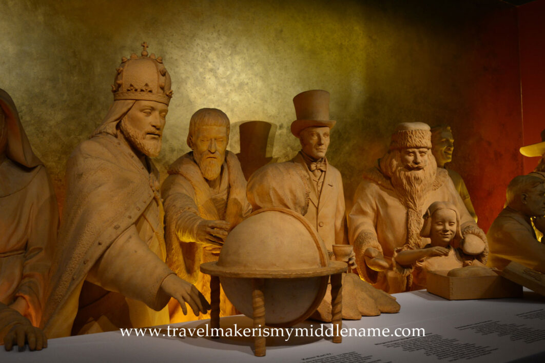 Life sized sculptures of people made from marzipan seated at a table looking at a globe at the free marzipan museum in the Niederegger shop in Lübeck. No touching allowed.