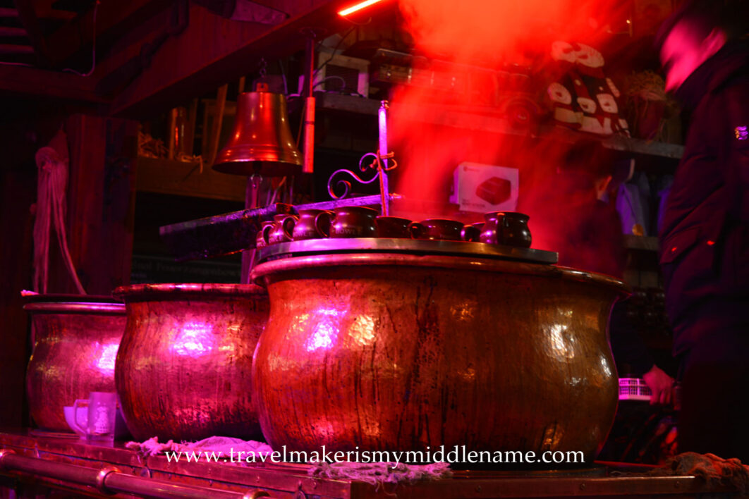 3 large copper pots of steaming glühwein with mugs on top