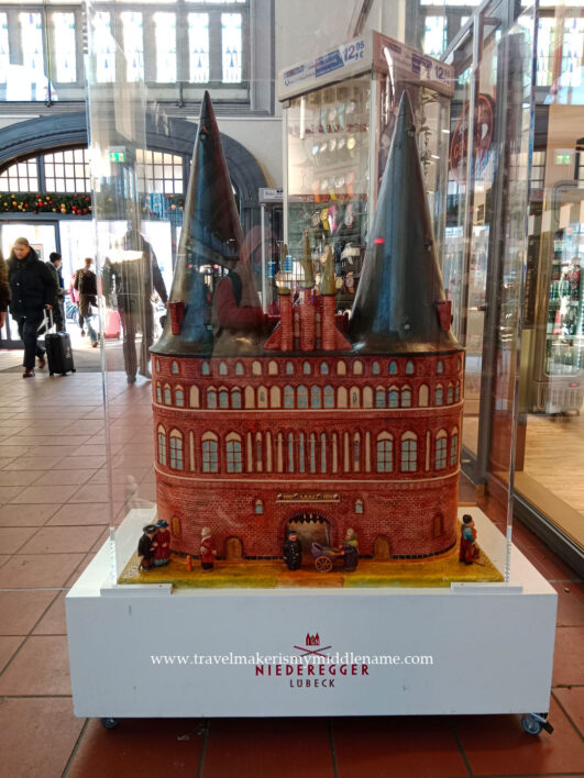 Marzipan model of the Holstentor with miniature pepole on a white Niederegger rolling platform.